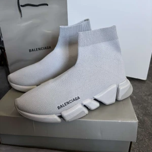 Grå Balenciaga Speed sneakers - Säljer ett par ljusgrå Balenciaga Speed sneakers med stickad ovandel och chunky sula. Skorna har en strumpliknande passform och Balenciaga-logga på sidan. Perfekta för dig som gillar modern och clean stil.