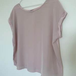 Ljusrosa blus i lös passform - Säljer en ljusrosa blus i lös passform med rund halsringning och korta ärmar. Tunt och lätt material som ger en luftig känsla, perfekt för varmare dagar. Enkel och stilren design som passar till många olika outfits.