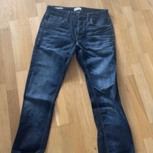 Mörkblå jeans från Jack & Jones - Säljer ett par mörkblå jeans från Jack & Jones med klassisk femficksdesign och kontrastsömmar. Jeansen har normal passform och raka ben, perfekta till vardags. Märkespatch bak i midjan och snygga slitningar framtill.