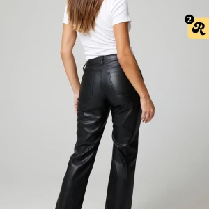 Svarta skinnbyxor med raka ben - Snygga svarta byxor i skinnimitation med raka ben och hög midja. Klassisk femficksmodell med diskreta sömmar och knapp- samt dragkedjestängning framtill. Perfekta för en trendig och stilren look.