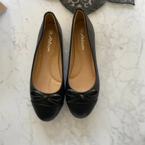 Svarta ballerinaskor med rosett från Abloom - Säljer ett par klassiska svarta ballerinaskor från Abloom. Skorna har en söt rosett framtill och rund tå.  