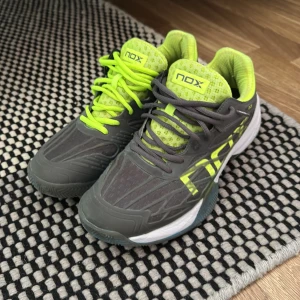 Grå och neongula padelskor från NOX - Säljer ett par padelskor från NOX i grått med neongula detaljer och snörning. Skorna har meshpartier för extra ventilation och en platt sula som ger bra grepp. Använda ett fåtal gånger men är i ett superskick!! Hör av er vid intresse. 