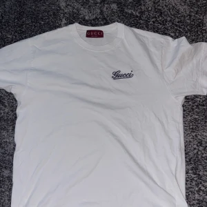 Vit t-shirt från Gucci - Mypris 5500kr, Säljer en klassisk vit t-shirt från Gucci med diskret broderad logga på bröstet. T-shirten har rund halsringning och korta ärmar. Perfekt för dig som gillar stilrena märkesplagg.