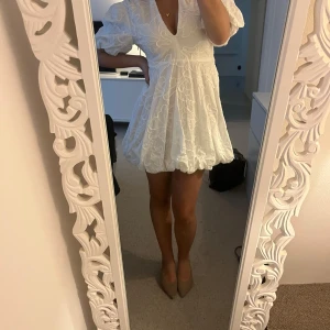Vit kortklänning med puffärm och broderade detaljer - Supersöt vit kortklänning med puffiga ärmar och v-ringning. Klänningen har broderade blommor och en volangig nederkant som ger extra volym. Perfekt för studenten, helt ny, säljer till väldigt bra pris så det är först till kvarn!