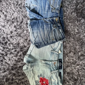 Två par jeansshorts - Två par jeansshorts i olika tvättar. Ett par är mörkblå med slitningar från Lee. Det andra paret är ljusblått med broderad röd ros framtill från Hollister.
