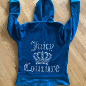 Blå hoodie ifrån Juicy Counture - Juicy Couture hoodie i blå velour med huva och dragkedja. Stor Juicy Couture-logga och krona på ryggen. 