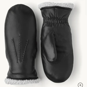 Svarta skinnvantar från Hestra - Svarta tumvantar i skinn från Hestra med mjukt, vitt fleecefoder. Klassisk design med elastisk handled och diskret logotyp. Perfekta för kalla vinterdagar. HELT OANVÄNDA lappen sitter kvar. Köpta för 1300kr. 