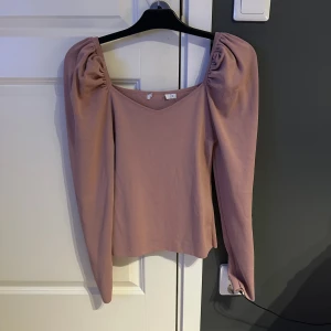 Ljusrosa topp med puffärmar från NA-KD - Trendig ljusrosa topp från NA-KD med långa puffärmar och fyrkantig ringning. Toppen har en mjuk och stretchig känsla, perfekt för att lyfta din outfit med en feminin touch.