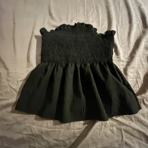 Svart smockad topp med volang - Supersöt svart topp med smockad överdel och volangdetalj vid halsen. Toppen har en luftig och lätt utsvängd nederdel, perfekt för varma dagar. Passar till både jeans och kjol.