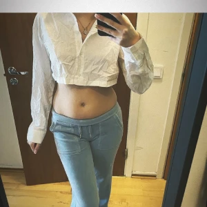 Vit croppad skjorta - Säljer en vit croppad skjorta med lång ärm och klassisk krage. Skjortan har en stilren och enkel design, perfekt att matcha med både jeans och kjol. Passformen är normal och materialet känns lätt och bekvämt. också oanvänd bara legat och skrotat💞