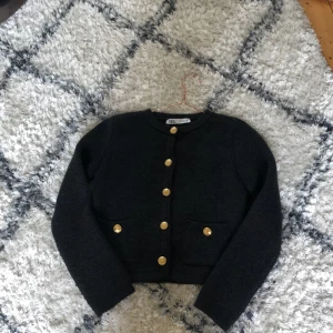 Svart cardigan med guldknappar från Zara - Säljer en svart stickad cardigan från Zara med rund halsringning och dekorativa guldknappar framtill. Den har två fickor fram och lång ärm. Perfekt för att lyfta en enkel outfit💕💕