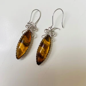 Vintage örhängen bärnsten - Snygga örhängen i silverfärgmed avlånga, bärnstenar och dekorativa snirkliga detaljer upptill. Hängande modell som ger ett elegant intryck och passar perfekt till att lyfta din stil.