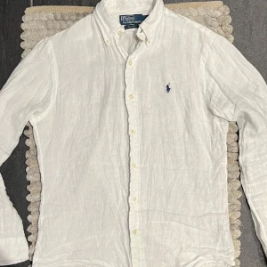 Ralph Lauren Linneskjorta Vit - Klassisk vit linneskjorta från Ralph Lauren i storlek S, men passar även dig som vanligtvis bär M. Skön och luftig – perfekt till sommaren. I fint skick förutom en liten slitning bredvid en av knapparna, vilket inte påverkar användningen. Passar lika bra till stranden som till en uppklädd vardag.  🔹 Märke: Ralph Lauren 🔹 Färg: Vit 🔹 Storlek: S (passar även M) 🔹 Material: 100% linne 🔹 Skick: Fint, liten slitning vid knapp 
