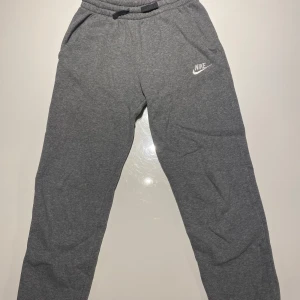 Grå mjukisbyxor från Nike - Snygga grå mjukisbyxor från Nike med klassisk logga på vänster ben. Byxorna har resår i midjan med dragsko och är tillverkade i mjukt material som är perfekt för chill eller träning. Raka ben och enkel design. I storlek 147-158 (L). Inga defekter och nästan aldrig använt. För ENDAST 150kr så får du de bästa gråa mjukisbyxorna från Nike!