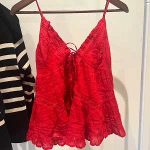 Röd volangig linnetopp med knyt - Säljer en röd linnetopp med tunna axelband och volangkant nertill. Toppen har knytning framtill