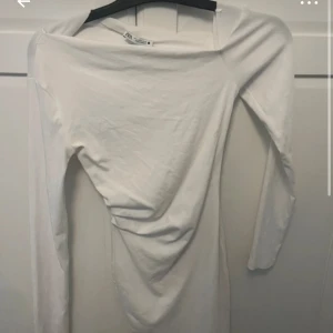 Vit långärmad kortklänning från Zara - Säljer en stilren vit långärmad klänning från Zara. Klänningen är tight och har en enkel, rak design med rund halsringning. Perfekt för dig som gillar minimalistisk stil.