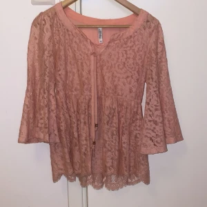 Rosa spetsblus från Chiara Forthi - Säljer en romantisk rosa spetsblus från Chiara Forthi med vackra vida ärmar och knytband framtill. Blusen har ett genombrutet spetsmönster och volangliknande nederdel. Perfekt för dig som gillar feminina detaljer!