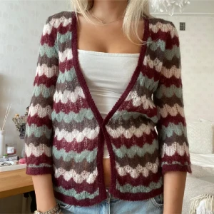 Mönstrad stickad kofta i flera färger - Säljer en mysig stickad kofta med vågigt mönster i vinrött, ljusrosa, grått och grönt. Koftan har trekvartsärm och öppen front utan knäppning. Perfekt att slänga över ett linne eller t-shirt för en cool lager-på-lager-look.