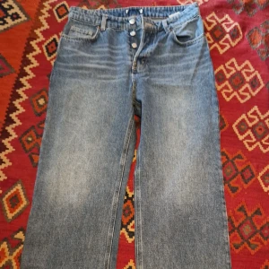 Blå raka jeans med knappar - Klassiska blå jeans med raka ben och knäppning framtill. Jeansen har fem fickor och en tidlös tvätt som passar till det mesta. Perfekta för dig som gillar en enkel och avslappnad stil.