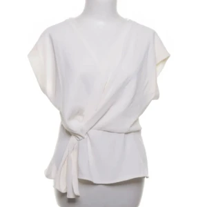 Vit omlottopp med knyt - Säljer en stilren vit omlottopp med knyt i midjan. Toppen har korta ärmar och en lös passform som ger en avslappnad men ändå elegant look. Perfekt att matcha med både jeans och kjol för en fräsch stil.