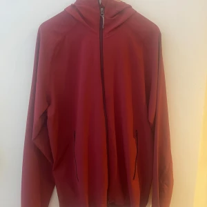 Röd hoodiejacka från Houdini - Säljer en röd hoodiejacka från Houdini i herrstorlek XL. Jackan har dragkedja framtill, två fickor med dragkedja och huva. Perfekt för lager-på-lager och passar bra till utomhusaktiviteter. Den har några knappt märkbara fläckar, skriv om ni vill ha bild på dem.