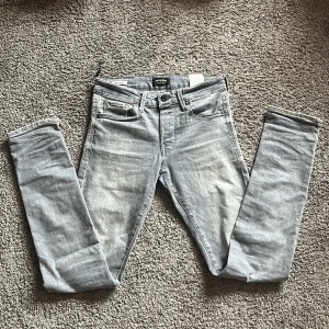 Ljusgrå slim jeans från Jack & Jones - Säljer ett par ljusgrå slim fit jeans från Jack & Jones, modell Glenn. Jeansen har klassisk femficksdesign, knappgylf och smal passform. Perfekta för dig som gillar en stilren och enkel look.