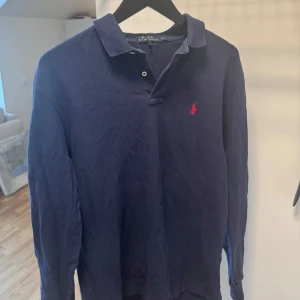 Marinblå långärmad pikétröja från Polo Ralph Lauren - Säljer en klassisk marinblå långärmad pikétröja från Polo Ralph Lauren. Skicket är väldigt bra och storleken är M