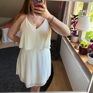 Vit klänning med smala axelband - Säljer en söt vit klänning med smala axelband och v-ringning. Klänningen har ett dubbelt lager upptill och öppen rygg med korsade band. Perfekt för sommarens alla tillfällen!