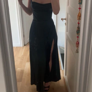 grön balklänning med slits - Säljer en elegant grön balklänning med axelbandslös design och hög slits på ena sidan. Klänningen har en figurnära passform upptill och faller snyggt längs kroppen. Perfekt för speciella tillfällen.