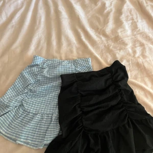 Två kjolar från Gina Tricot, svart och blå/vit-rutig - Säljer två snygga kjolar från Gina Tricot i storlek XS. En är svart med rynkade detaljer och volang, den andra är blå och vit med rutigt mönster, också med rynk och volang. Perfekta för dig som gillar trendiga kortkjolar! De kan köpas styckvis också! Pris kan diskuteras 