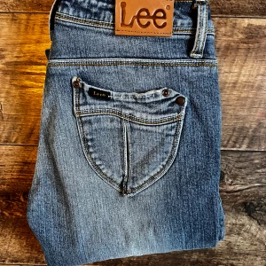 Blå jeansbyxor från Lee - Snygga blå jeans från Lee med klassisk femficksdesign och slitna detaljer på benen. Byxorna har normal passform och är tillverkade i bomull med lite elastan för extra komfort. Perfekta för en avslappnad stil.