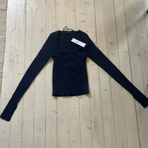 Mörkblå ribbad topp från Gina tricot  - Säljer en mörkblå ribbad topp från Gina tricot i storlek XS. Tröjan har lång ärm och en tight passform med en snygg asymmetrisk halsringning. Perfekt för dig som gillar stilrena och trendiga plagg.
