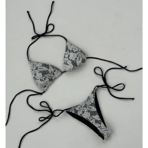 Svart och vit spetsbikini med knyt - Snygg bikini från design by si med svart och vit spetsdetalj. Klassisk trekantsmodell med knyt både i rygg och vid höfter. Perfekt för sommardagar på stranden. Topp och trosa i matchande design. (Helt oanvänd säljer då den var för liten och försent att skicka tillbaka) 