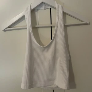 Vit ribbad halterneck topp från H&M Divided - Säljer en vit ribbad halterneck topp från H&M Divided. Toppen har ärmlös design och rundad djup urringning fram. Perfekt för varma dagar eller som lager under skjorta.