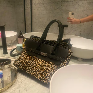 Leopardmönstrad Birkin  - Säljer en snygg leopardmönstrad handväska med svarta handtag och detaljer. Väskan har en dragkedja och ett stilrent spänne framtill. Perfekt för att ge din outfit en djärv touch! 🐆🖤