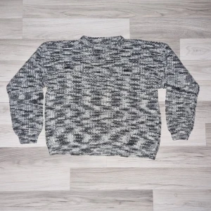Gråmelerad hemmastickad tröja - Säljer en mysig gråmelerad hemmastickad tröja med lång ärm. Perfekt för kyliga dagar med sitt mjuka material och avslappnade passform. Tröjan har en ribbad struktur som ger extra stil och komfort.