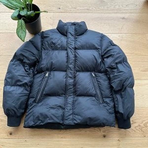 Svart pufferjacka från Arket - Säljer en svart pufferjacka från Arket i storlek M. Jackan har en hög krage och dragkedja framtill. Den är quiltad och har långa ärmar med ribbade muddar. Perfekt för kyliga dagar.