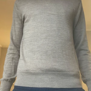 Grå tröja från Sandö - Säljer en stilren grå tröja från Sandö i storlek S. Tröjan har långa ärmar och en klassisk design som passar perfekt till vardags. Den är tillverkad i ett mjukt material som ger en bekväm känsla.