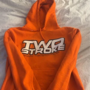 Two stroke hoodie - Säljer en cool orange hoodie från Gildan med trycket 'Two Stroke' på framsidan. Perfekt för en avslappnad stil med sin bekväma passform och klassiska design. Hoodie med känguruficka och justerbar huva.