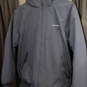 Blå vindjacka från Carhartt - Säljer en stilren blå vindjacka från Carhartt. Köpt för 2000kr på zalando om jag minns rätt. Men kan släppa den för 1300kr. Skriv vid fler bilder eller funderingar:)