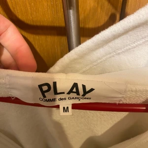 Vit hoodie från Comme des Garçons - Säljer en stilren vit hoodie från Comme des Garçons med det ikoniska röda hjärtat på bröstet. Tröjan kan vara lite liten i passformen, så storlek M som det är kan även passa dig med storlek S.