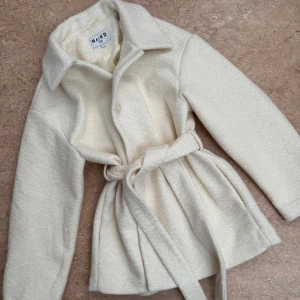 Vit kappa från NA-KD - Säljer en vit oanvänd kappa från NA-KD. Den har knäppning framtill samt ett bälte i midjan för en snygg passform. 