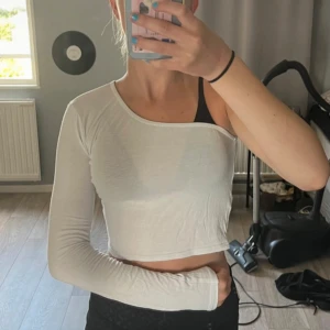 Vit oneshoulder topp - Säljer en stilren vit oneshoulder topp med lång ärm. Toppen är croppad och har en tight passform, perfekt för en trendig look. Passar bra till både jeans och kjol. Perfekt för sommarens varma dagar!
