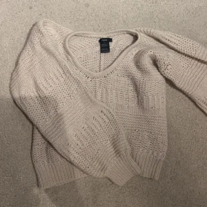 Beige stickad tröja från Filippa K - Säljer en snygg beige stickad tröja från Filippa K. Tröjan har en v-ringad design och långa ärmar, perfekt för kyligare dagar. Den är tillverkad i en mjuk och bekväm ullblandning som håller dig varm och stilren.