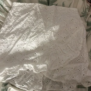 Vit broderad kortkjol - Säljer en söt vit kortkjol med broderade detaljer och volangkant. Perfekt för sommarens varma dagar. Kjolen har en omlott-design som ger en fin passform. Passar bra till både sneakers och sandaler.