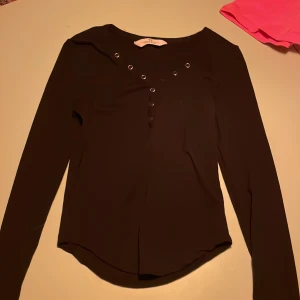 Svart långärmad topp från H&M - Snygg svart långärmad topp från H&M med dekorativa knappar. Toppen har en rund halsringning och är tillverkad i ett mjukt material för extra komfort.