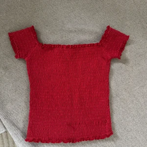 Röd ribbad topp - Säljer en snygg röd ribbad topp med korta ärmar och en offshoulder-design. Perfekt för en trendig look. Passar bra till både jeans och kjol. Hör av dig vid intresse!