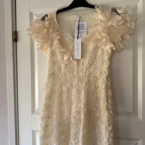 Krämfärgad klänning från Ida Sjöstedt - Helt ny klänning från Ida Sjöstedt. Lapparna kvar. Aldrig använd. Elissa Dress heter klänningen. Storlek 36.  Perfekt nu inför student. Studentklänning. Eller perfekt för bröllopsfesten! Bröllopsklänning.  Nypris 4199kr Köpte den till min student men valde tillslut en annan klänning.Säljer en vacker krämfärgad klänning från Ida Sjöstedt med blommiga detaljer och volanger. Klänningen har en v-ringad design och korta ärmar med volangdetaljer. Perfekt för speciella tillfällen! 🌸