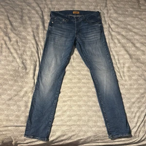 Blå slim/glenn jeans från Jack & Jones - Snygga blå slim jeans från Jack & Jones med en klassisk femficksdesign. De har en lätt tvättad look och är perfekta för en stilren vardagsoutfit. Märkta med 'Slim/Glenn' på insidan.