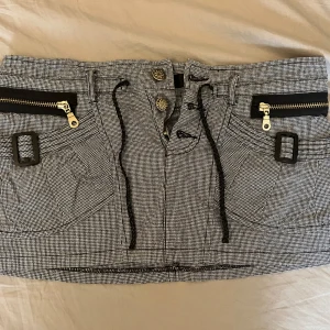 Grå lågmidjad minikjol med dragkedjor - Snygg kortkjol med coola dragkedjor och knappar framtill. Kjolen har praktiska fickor och ett justerbart knytband i midjan. Perfekt för en trendig look! Säljer då den inte kom till användning, kan skicka fler bilder vid behov. Midjemått ca 78 cm (jag har storlek S och den passar mig)